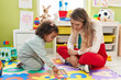 © Krakenimages.com - Teacher and toddler playing with maths puzzle game sitting on floor at kindergarten