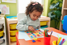 Adorable Hispanic Girl Playing With Maths Puzzle Game Sitting On Table At Kindergarten