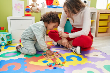 Sticker - Teacher and toddler playing with maths puzzle game sitting on floor at kindergarten