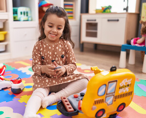 Poster - Adorable hispanic girl sitting on floor playing with mechanic toy at kindergarten