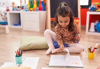 Sticker - Adorable hispanic girl preschool student sitting on floor drawing on notebook at kindergarten