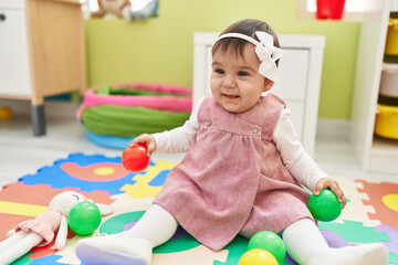 Sticker - Adorable hispanic baby playing with balls sitting on floor at kindergarten