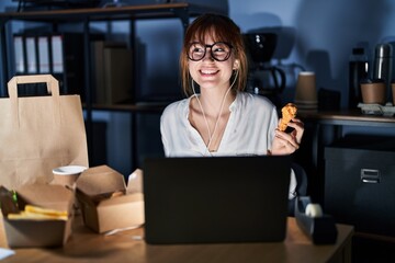 Wall Mural - Young beautiful woman working using computer laptop and eating delivery food smiling looking to the side and staring away thinking.