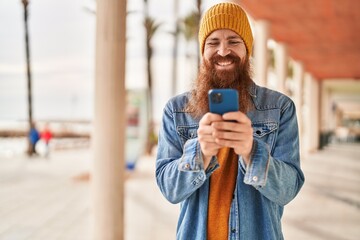 Wall Mural - Young redhead man smiling confident using smartphone at street