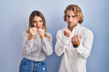 Sticker - Young couple standing over blue background ready to fight with fist defense gesture, angry and upset face, afraid of problem