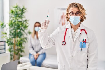 Wall Mural - Blond man wearing doctor uniform and medical mask holding syringe scared and amazed with open mouth for surprise, disbelief face
