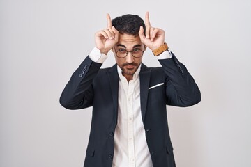 Sticker - Handsome business hispanic man standing over white background doing funny gesture with finger over head as bull horns