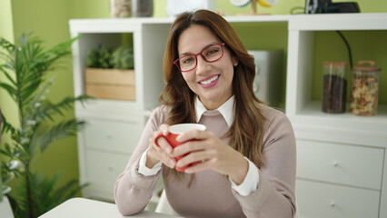 Poster - Young beautiful hispanic woman drinking coffee sitting on table at home