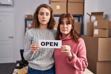 Wall Mural - Two women working at small business ecommerce holding open banner relaxed with serious expression on face. simple and natural looking at the camera.