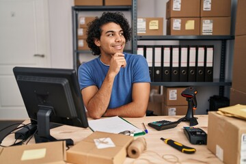 Poster - Hispanic man with curly hair working at small business ecommerce with hand on chin thinking about question, pensive expression. smiling and thoughtful face. doubt concept.