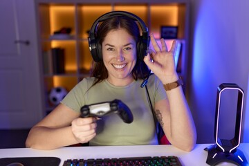 Canvas Print - Beautiful brunette woman playing video games wearing headphones smiling positive doing ok sign with hand and fingers. successful expression.