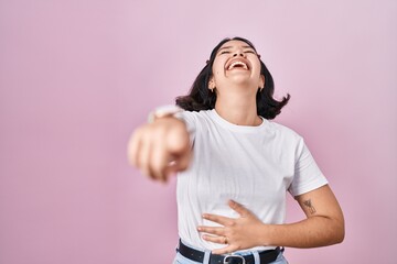 Sticker - Young hispanic woman wearing casual white t shirt over pink background laughing at you, pointing finger to the camera with hand over body, shame expression