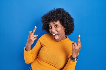 Poster - Black woman with curly hair standing over blue background showing middle finger doing fuck you bad expression, provocation and rude attitude. screaming excited