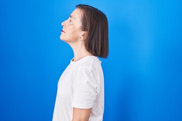 Wall Mural - Middle age hispanic woman standing over blue background looking to side, relax profile pose with natural face and confident smile.