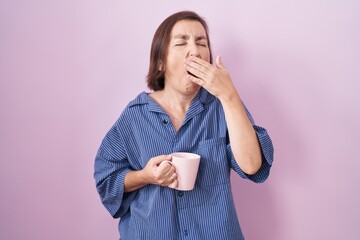 Poster - Middle age hispanic woman drinking a cup coffee bored yawning tired covering mouth with hand. restless and sleepiness.