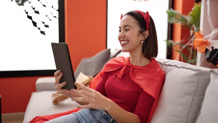 Canvas Print - Young beautiful hispanic woman wearing devil costume using touchpad at home