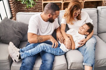 Wall Mural - Family doing tickle to son sitting on sofa at home