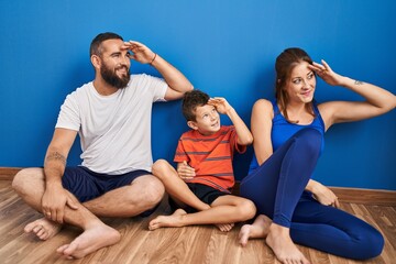 Sticker - Family of three sitting on the floor at home very happy and smiling looking far away with hand over head. searching concept.