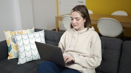 Sticker - Young blonde woman using laptop sitting on sofa at home