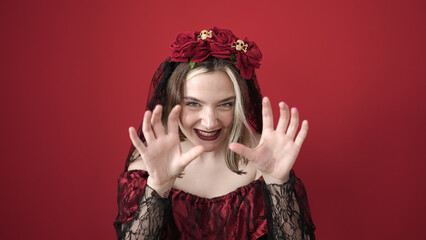 Wall Mural - Young blonde woman wearing katrina costume doing scare gesture over isolated red background