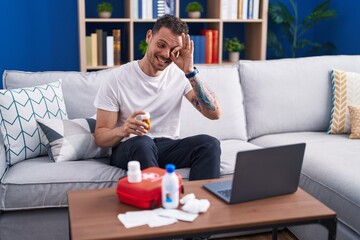 Poster - Young hispanic man watching video on laptop on how to use first aid kit smiling happy doing ok sign with hand on eye looking through fingers