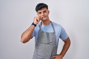 Sticker - Hispanic young man wearing apron over white background mouth and lips shut as zip with fingers. secret and silent, taboo talking