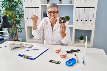 Poster - Middle age dentist woman holding chocolate doughnut smiling looking confident at the camera with crossed arms and hand on chin. thinking positive.