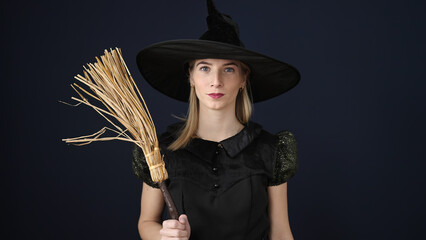 Poster - Young blonde woman wearing witch costume holding broom over isolated black background