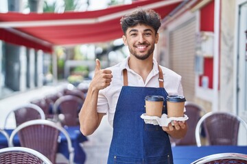 Poster - Arab man with beard wearing waiter apron at restaurant terrace smiling happy and positive, thumb up doing excellent and approval sign