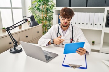 Poster - Young arab man wearing doctor uniform having video call at clinic