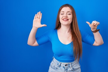 Poster - Redhead woman standing over blue background showing and pointing up with fingers number six while smiling confident and happy.