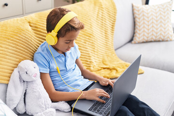 Canvas Print - Adorable hispanic boy using laptop and headphones sitting on sofa at home
