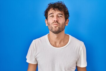 Poster - Hispanic young man standing over blue background looking at the camera blowing a kiss on air being lovely and sexy. love expression.