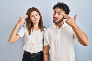 Canvas Print - Young couple wearing casual clothes standing together shooting and killing oneself pointing hand and fingers to head like gun, suicide gesture.