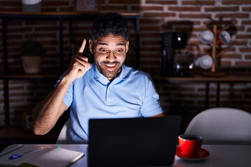 Canvas Print - Hispanic man with beard using laptop at night pointing finger up with successful idea. exited and happy. number one.