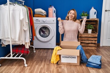 Canvas Print - Hispanic woman putting clothes in donation box screaming proud, celebrating victory and success very excited with raised arms