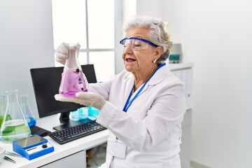 Wall Mural - Senior grey-haired woman wearing scientist uniform holding test tube at laboratory