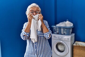 Wall Mural - Senior grey-haired woman smiling confident smelling cleaning t shirt at laundry room