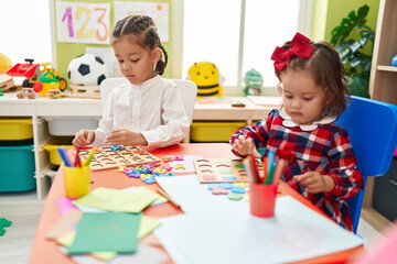 Brother and sister playing with maths puzzle game sitting on table at kindergarten