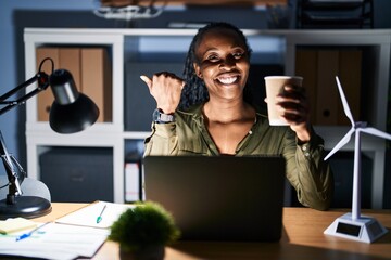 Canvas Print - African woman working using computer laptop at night pointing to the back behind with hand and thumbs up, smiling confident