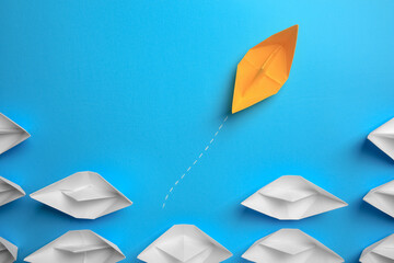 Poster - Yellow paper boat floating away from others on light blue background, flat lay. Uniqueness concept