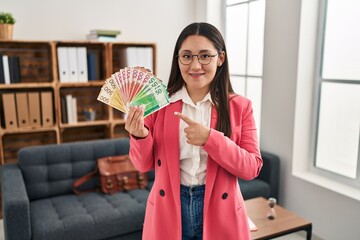 Wall Mural - Young latin woman working at consultation office holding money smiling happy pointing with hand and finger