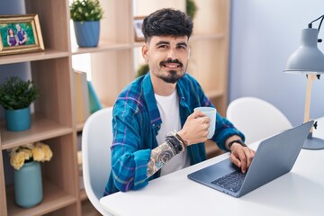 Sticker - Young hispanic man using laptop and drinking coffee at home