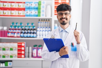 Wall Mural - Young hispanic man pharmacist smiling confident holding clipboard at pharmacy