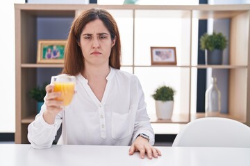 Wall Mural - Brunette woman drinking glass of orange juice skeptic and nervous, frowning upset because of problem. negative person.