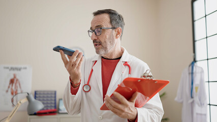 Wall Mural - Middle age man doctor sending audio message reading medical report at clinic