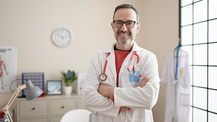 Canvas Print - Middle age man doctor smiling confident standing with arms crossed gesture at clinic