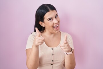 Canvas Print - Young hispanic woman standing over pink background pointing fingers to camera with happy and funny face. good energy and vibes.