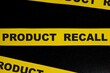 Product recall alert, caution and warning concept. Yellow barricade tape with word in dark black background.
