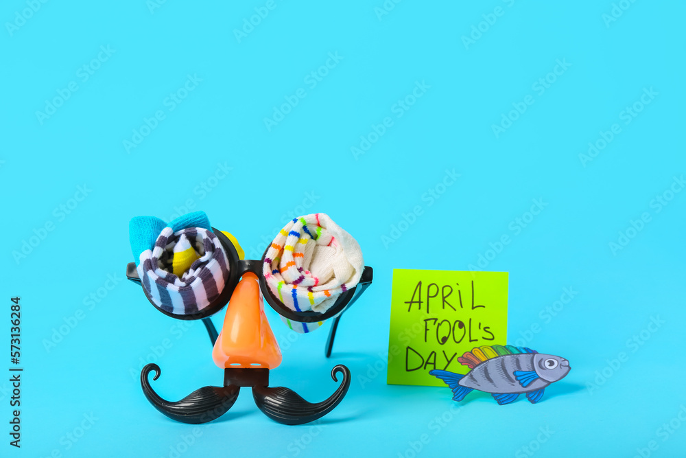 Eyeglasses, rolled socks and sticky note with text APRIL FOOL'S DAY on color background